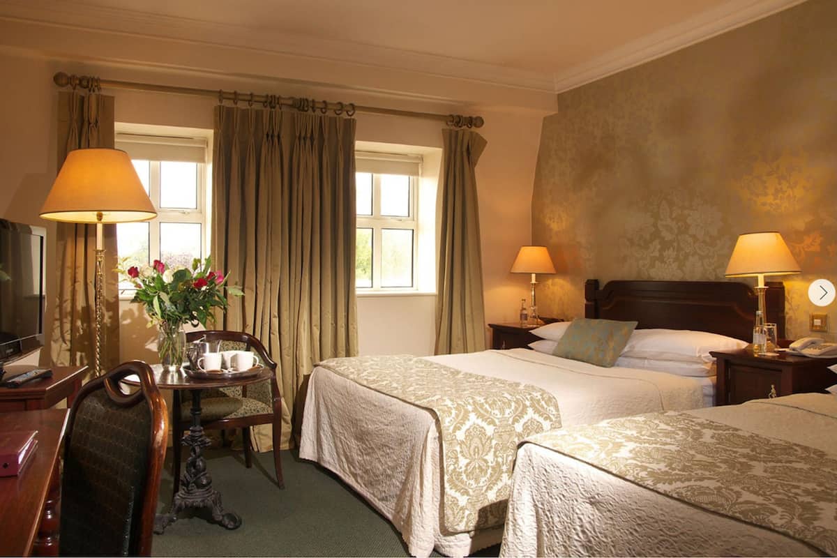 A hotel room with two beds, a desk with a chair, a television, and lamps.