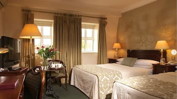 A hotel room with two beds, a desk with a chair, a television, and lamps.
