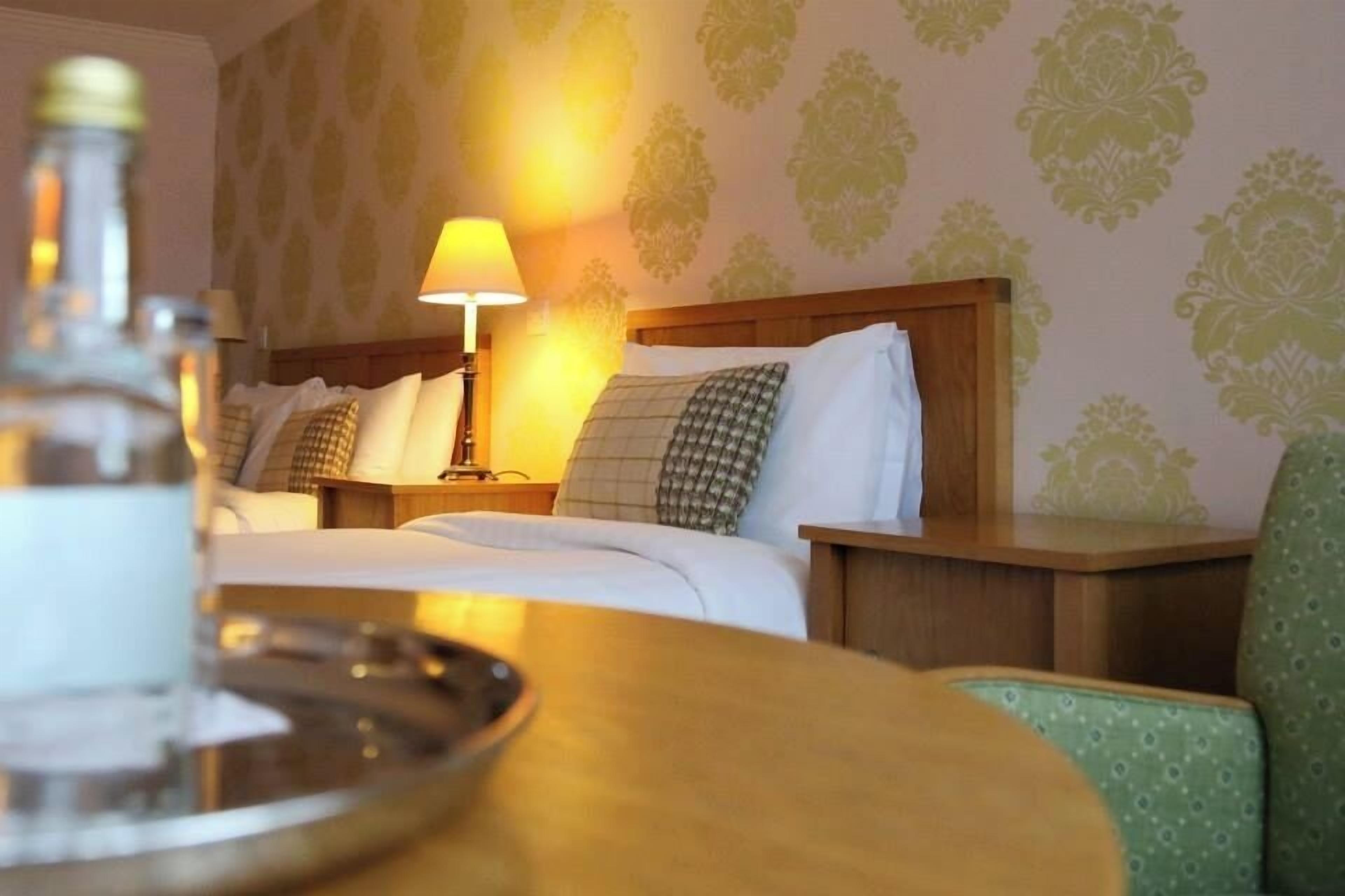 A hotel room with two beds, a nightstand with a lamp, and a green chair.