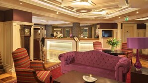A lobby with a purple sofa, striped armchairs, a reception desk, and a stone accent wall. - Castle Hotel Macroom (Macroom)