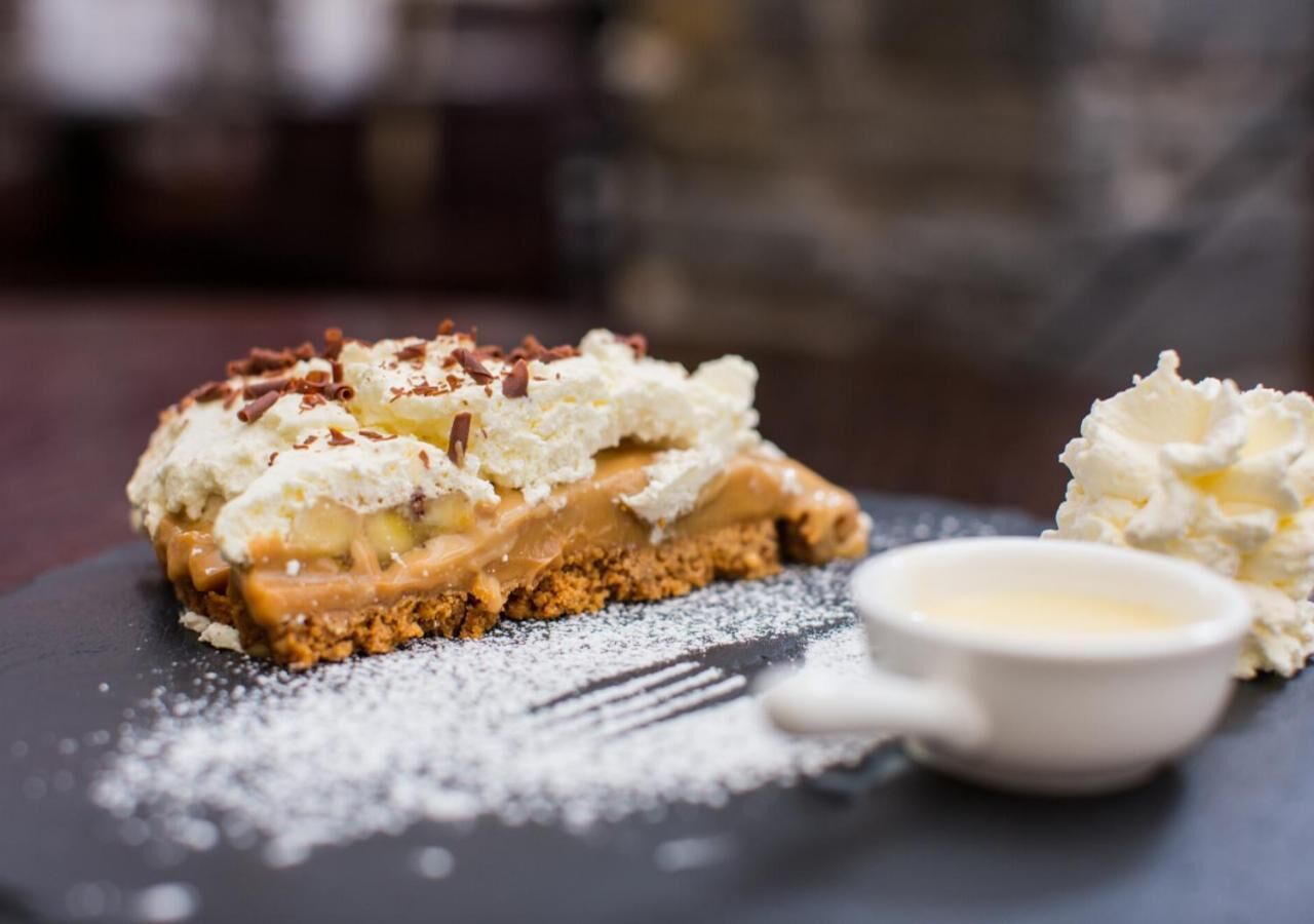 A dessert with a crumbly base, topped with whipped cream and a caramel-like sauce, accompanied by a small bowl of whipped cream.