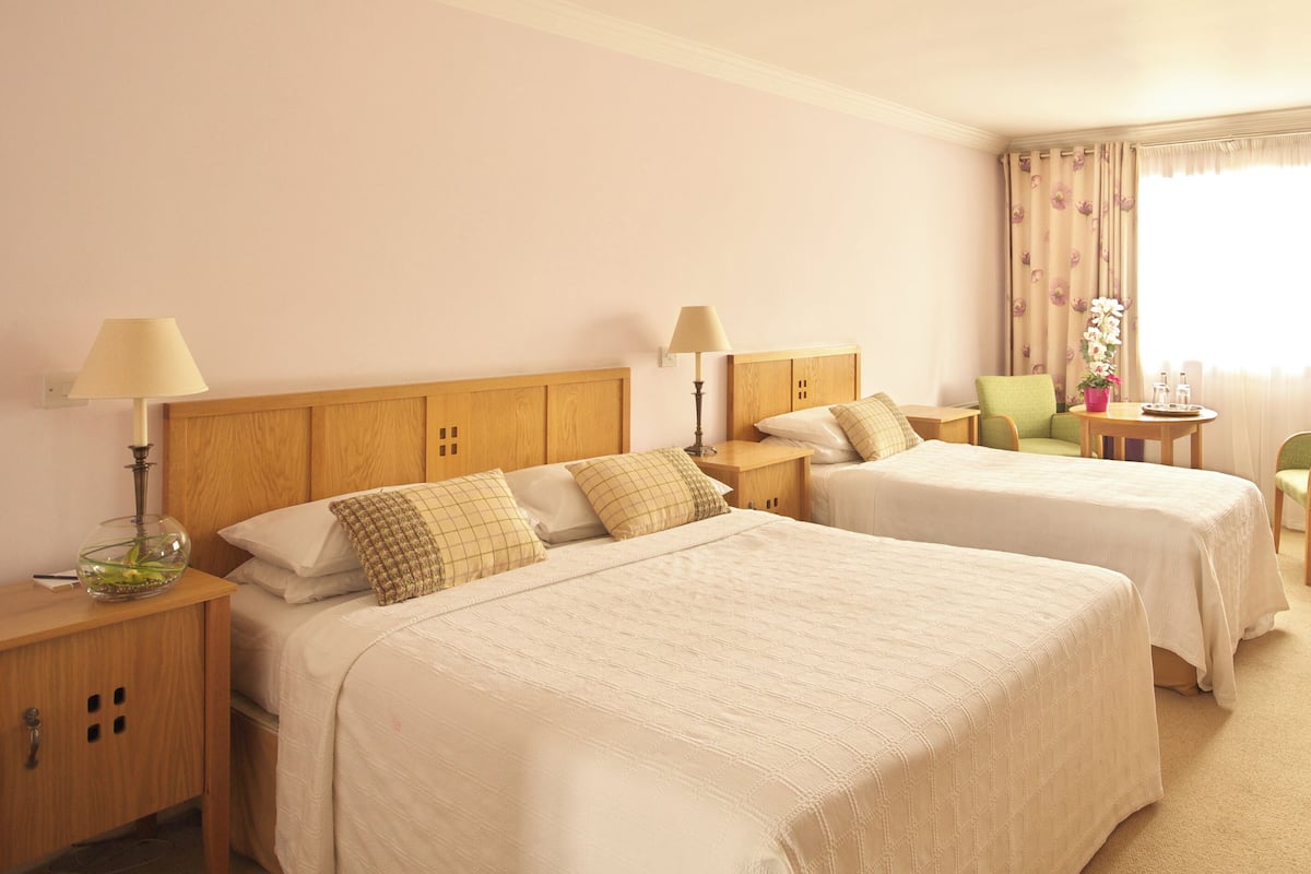 A hotel room with two beds, a desk, a chair, and a large window with curtains.