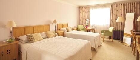 A hotel room with two beds, a desk, a chair, and a large window with curtains.