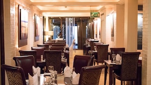 Un restaurant avec plusieurs tables et chaises, un mur en briques et des œuvres d’art encadrées accrochées au mur.