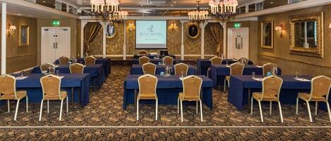 Una sala conferenze con tavoli e sedie, uno schermo per proiettore e lampadari.