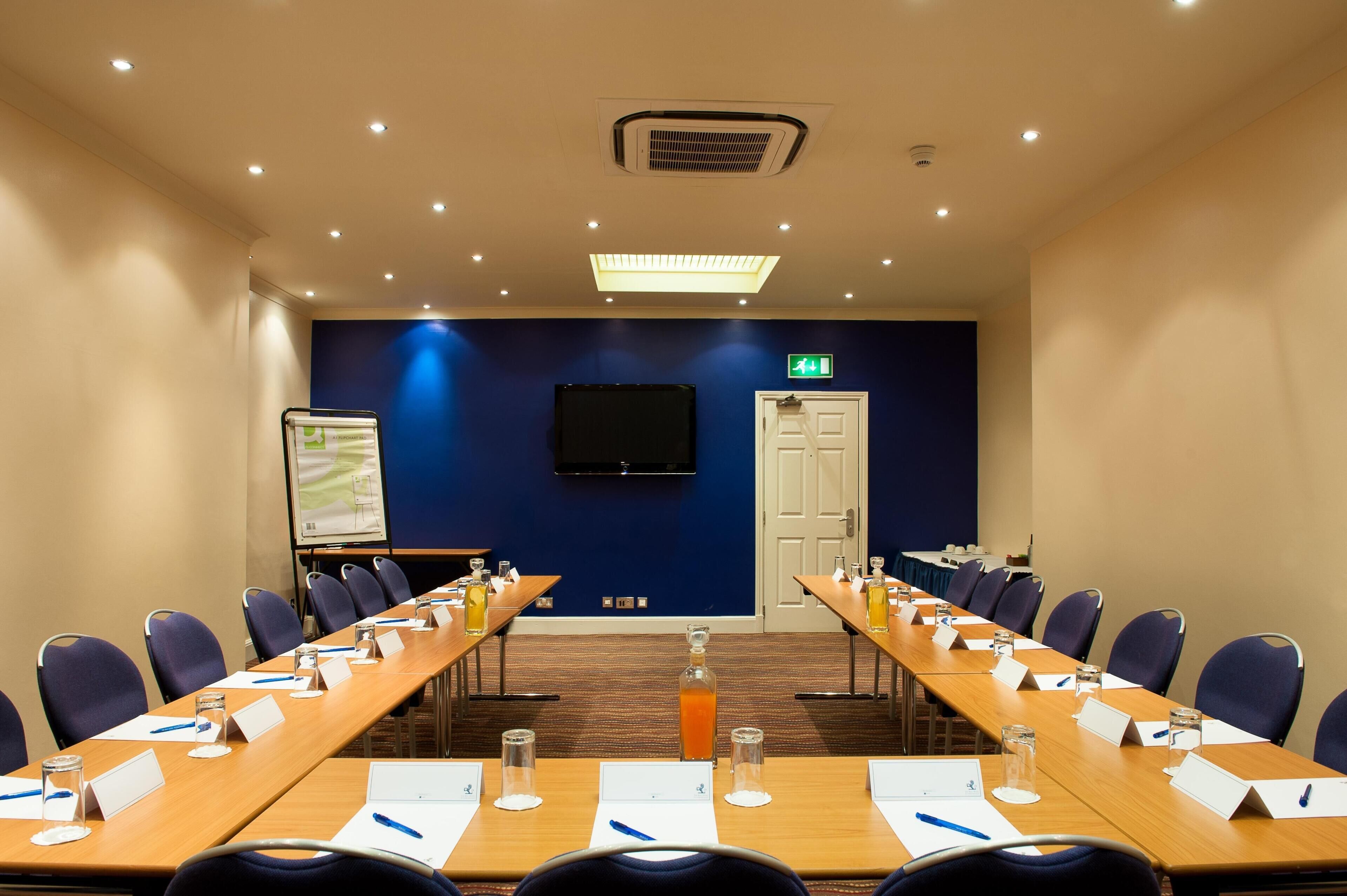 A conference room with long tables, chairs, nameplates, and a projector screen.