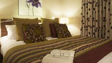 A neatly made bed with a striped bedspread, two pillows with leaf patterns, and a book with glasses on it.