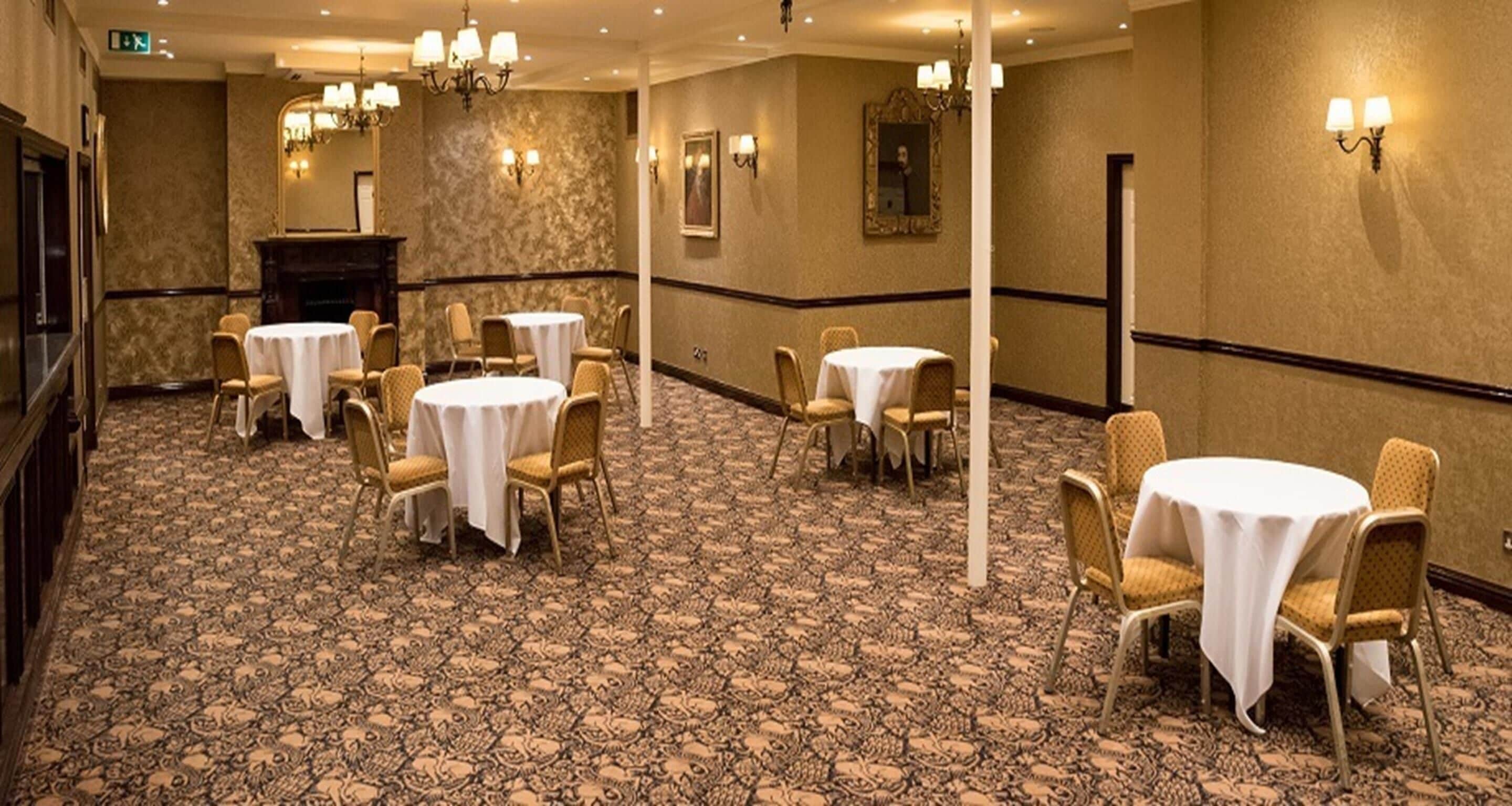 A hotel room with a carpeted floor, round tables with chairs, a fireplace, and wall sconces.