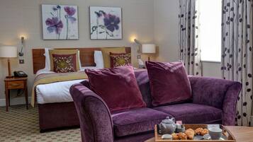 A hotel room with a bed, purple sofa, and a tray with pastries and tea set.