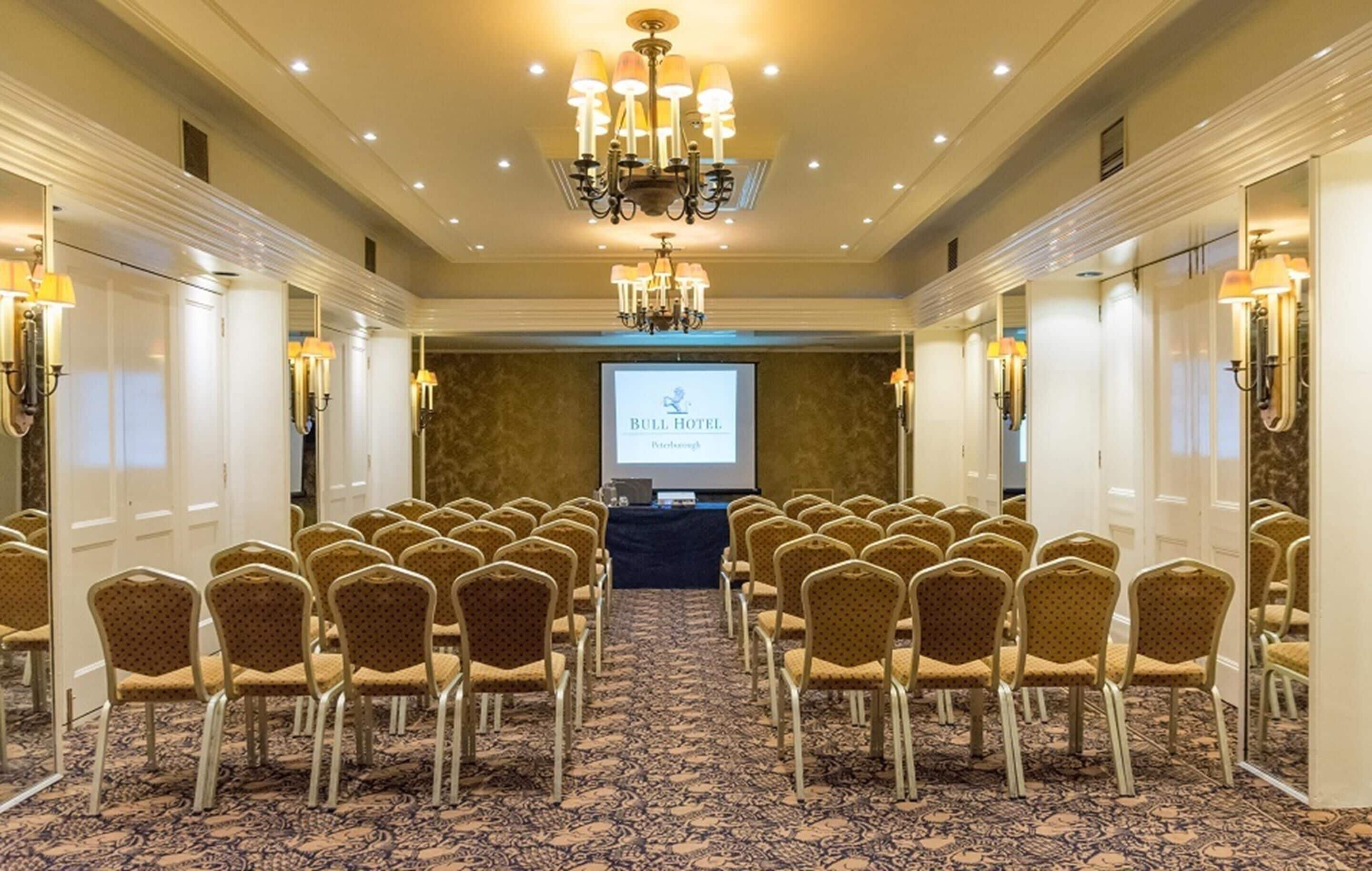 Une salle de conférence avec des rangées de chaises, un écran de projection et un lustre.
