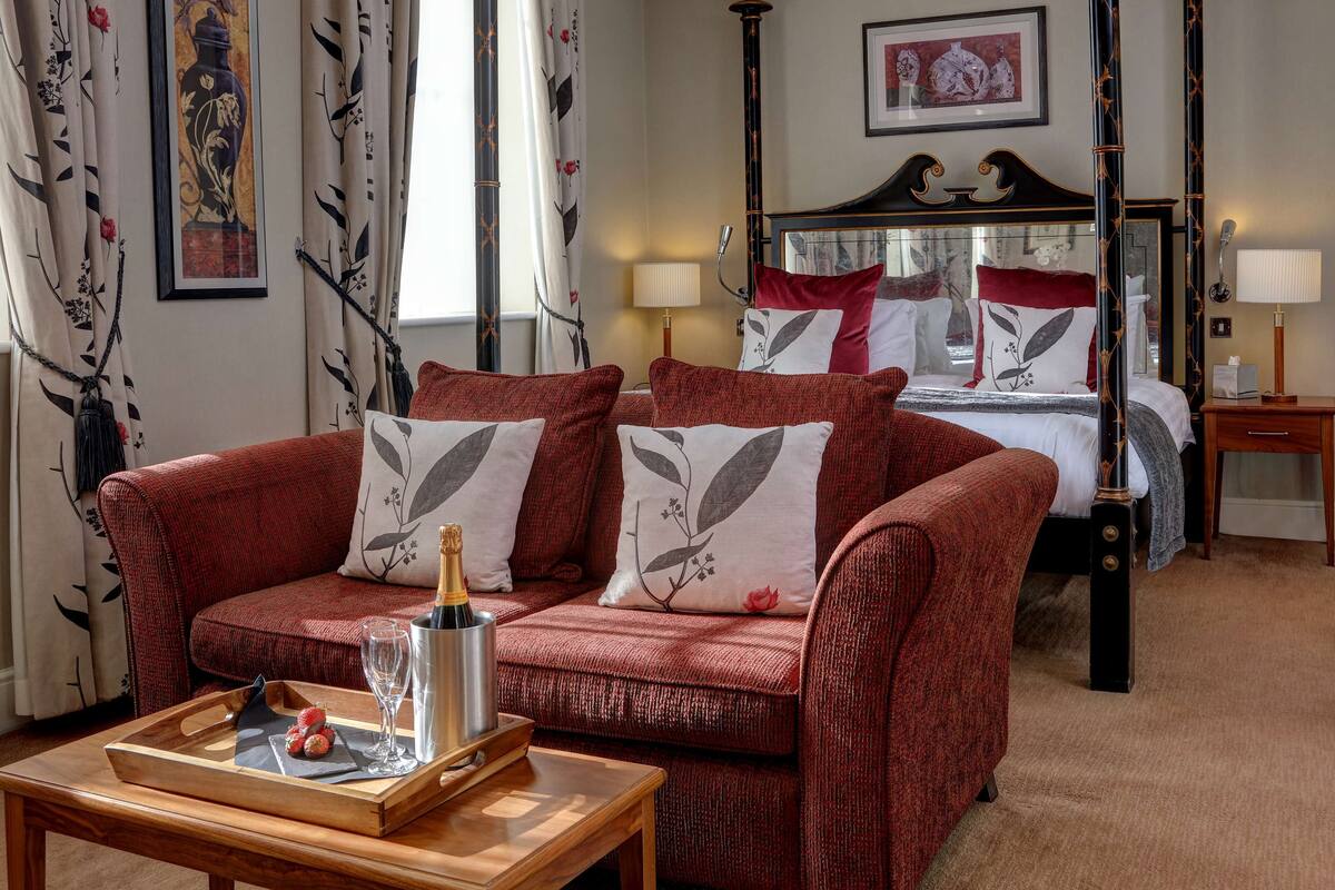 A hotel room with a red sofa, a bed with a canopy, and a wooden coffee table with a tray of food and drinks.
