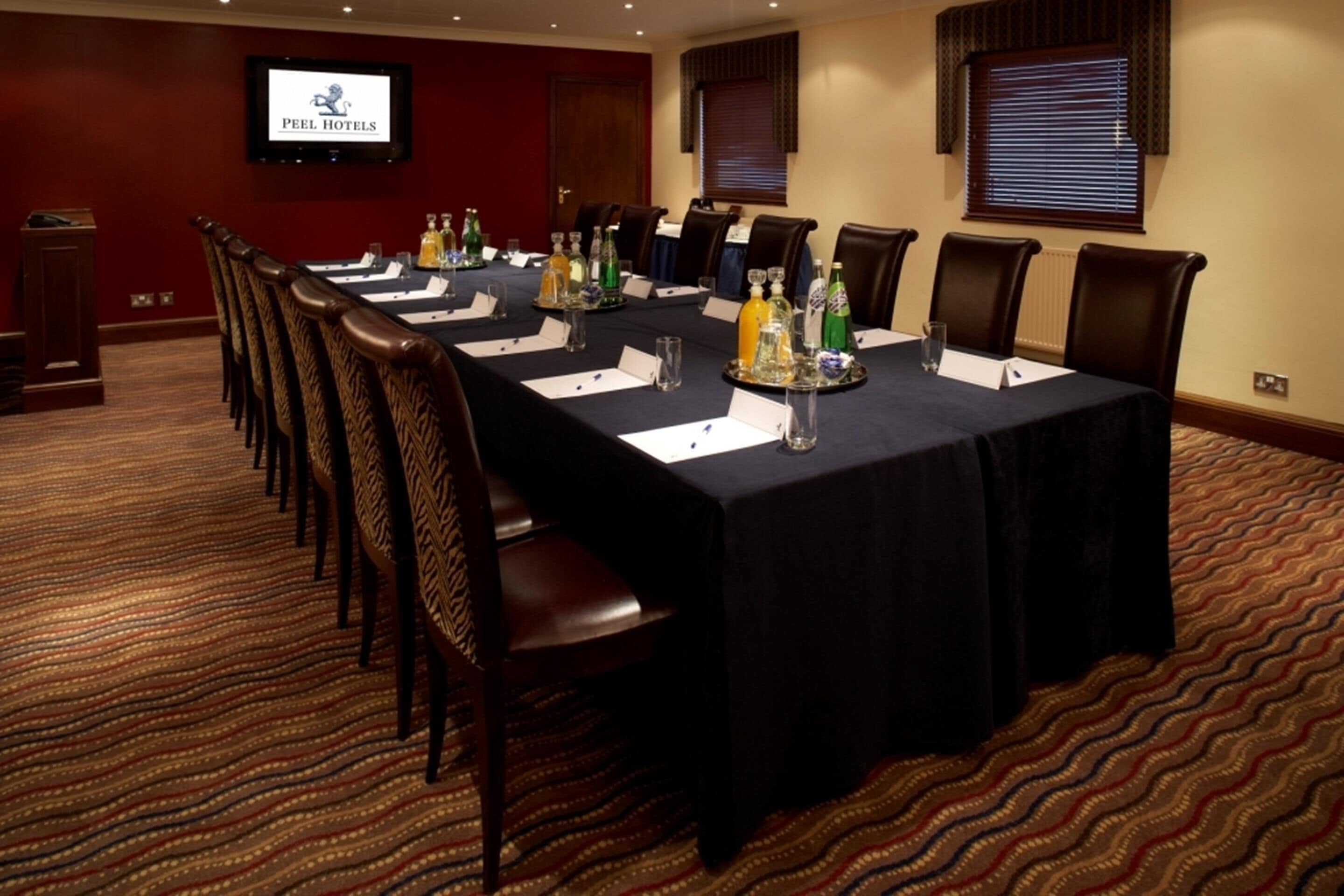 A conference room with a long table, chairs, name cards, and a television screen displaying 'PEEL HOTELS'.