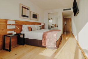 Ein Hotelzimmer mit einem hölzernen Kopfteil, einem Bett mit einem gemusterten Überwurf, einem Nachttisch mit einer Lampe und einem flachbildfernseher an der Wand.