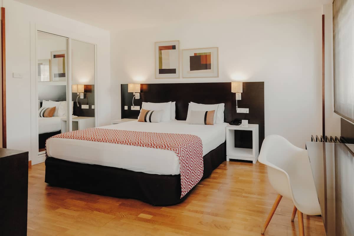 A modern hotel room with a large bed, bedside tables, a chair, and artwork on the walls.