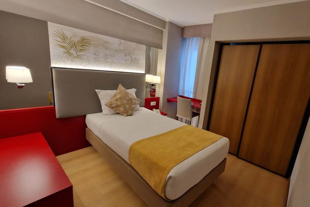 Habitación de hotel con cama, escritorio, silla, armario y televisión instalada en la pared.