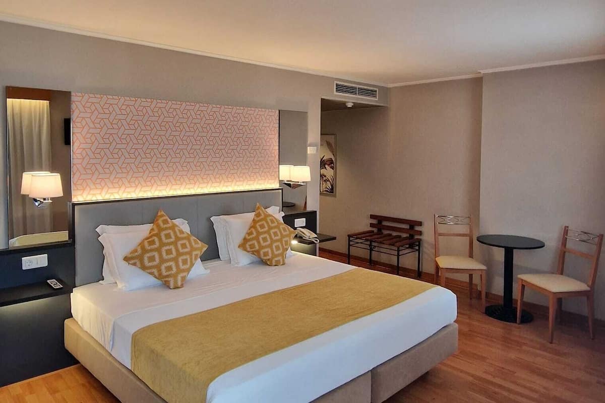 Una habitación de hotel con una cama grande, mesitas de noche, un escritorio y una silla.