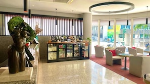 A modern lobby with a reception desk, seating area, and a bar with various beverages.