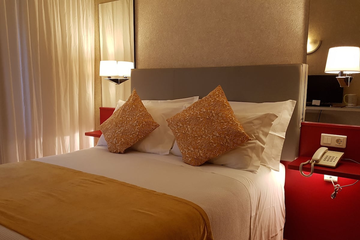 Habitación de hotel con una cama, dos almohadones decorativos, una mesita de noche con una lámpara y un teléfono.
