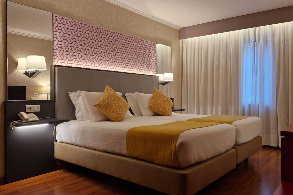 Una habitación de hotel con una cama grande, dos mesitas de noche, un escritorio y una ventana con cortinas.
