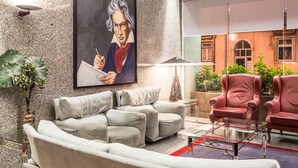 Un vestíbulo moderno con un cuadro grande, un sofá gris, un sillón rojo y una mesa de centro de vidrio.