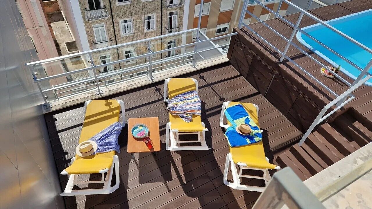A rooftop terrace with three sun loungers, a small table with a hat, and a pool.