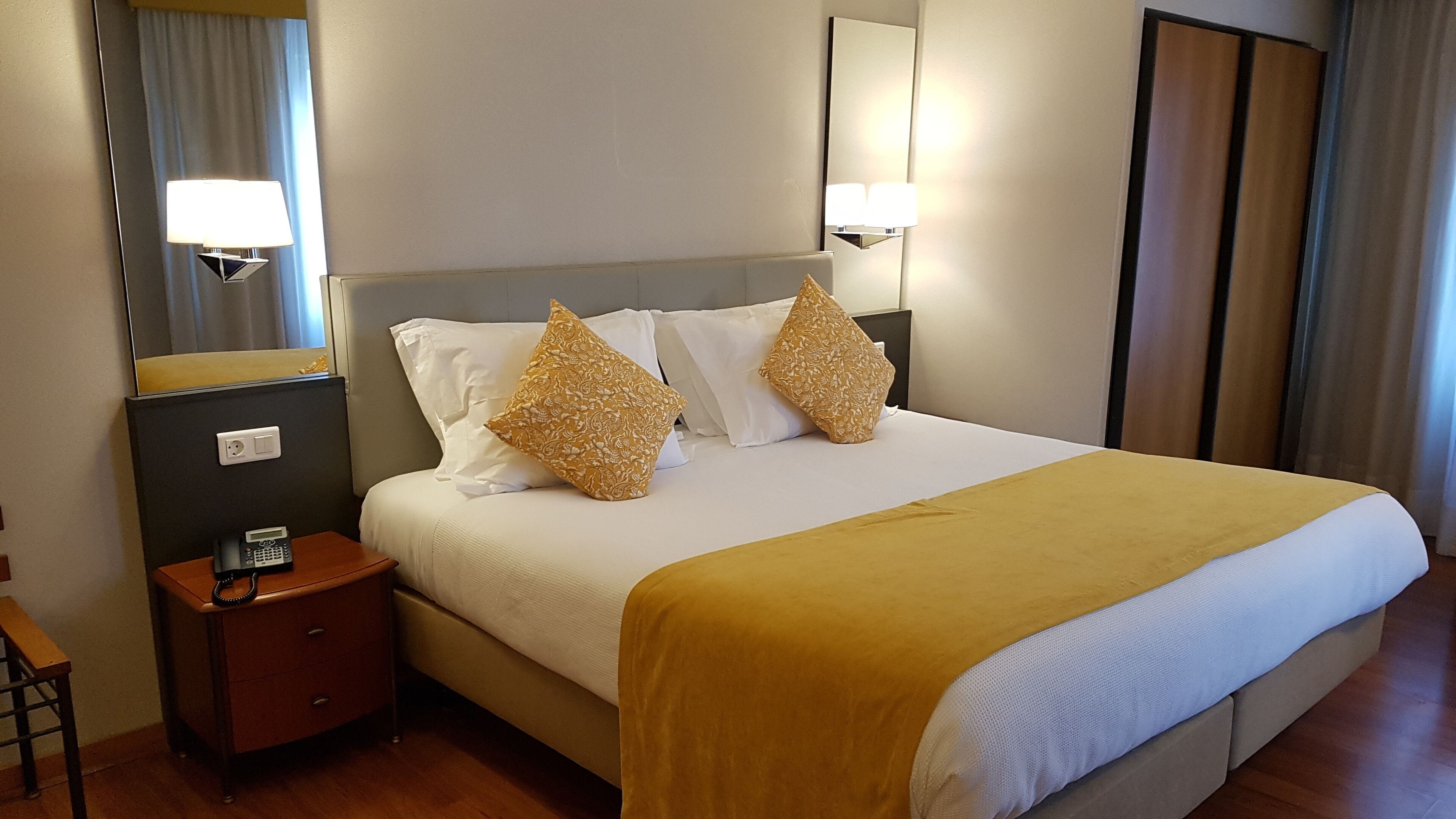 A hotel room with a bed, bedside table, lamp, and a mirror.