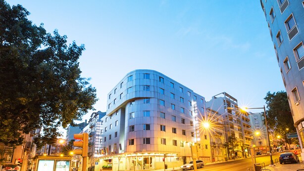 Un hotel moderno con fachada curva, varios pisos y una entrada bien iluminada.