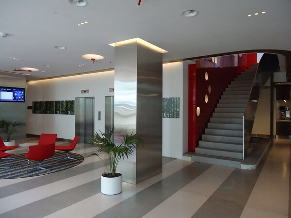 A modern lobby with a staircase, elevators, and red chairs. - Hotel Ambassador (Bern)