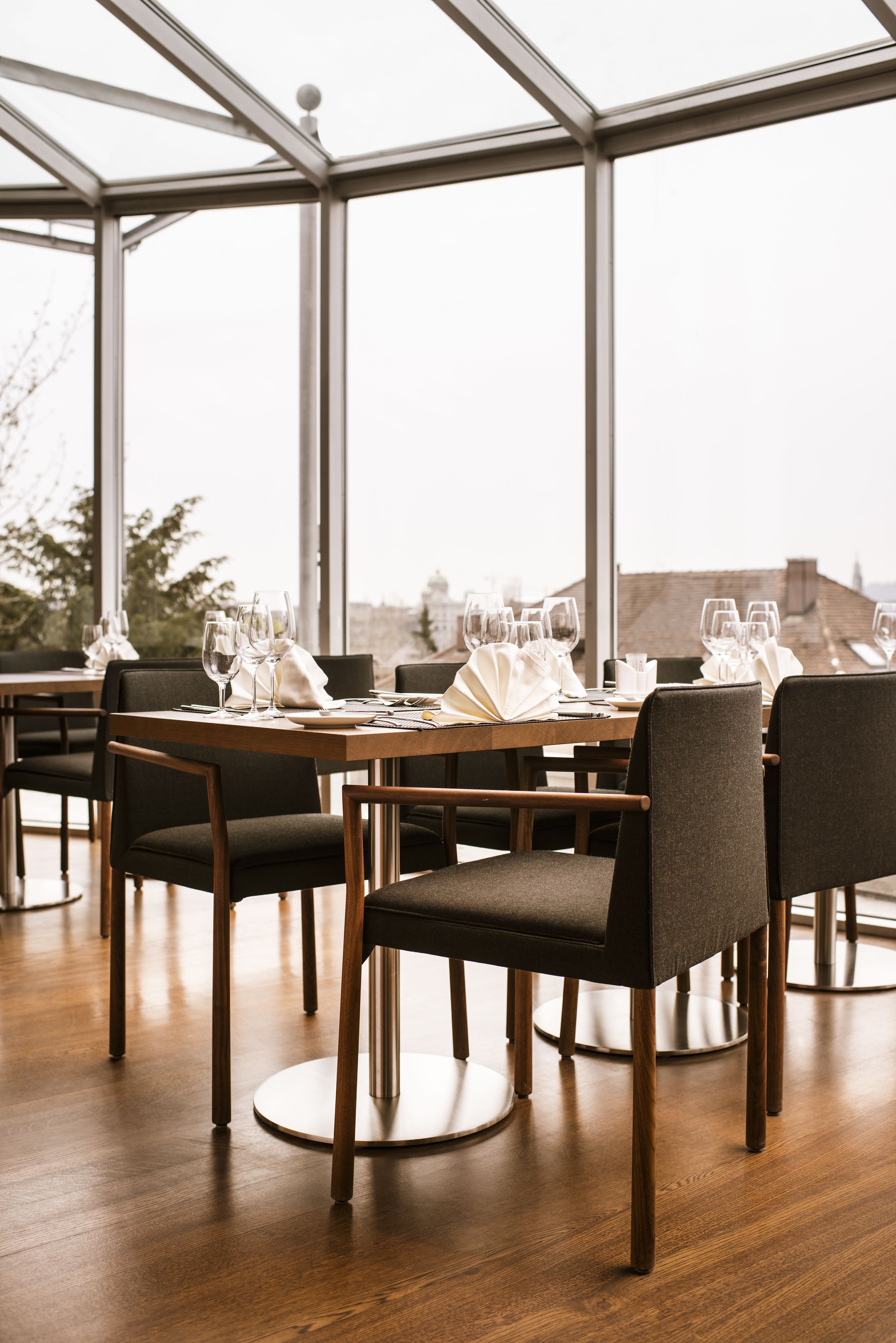 A restaurant with tables set for dining, large windows, and a view of the cityscape.