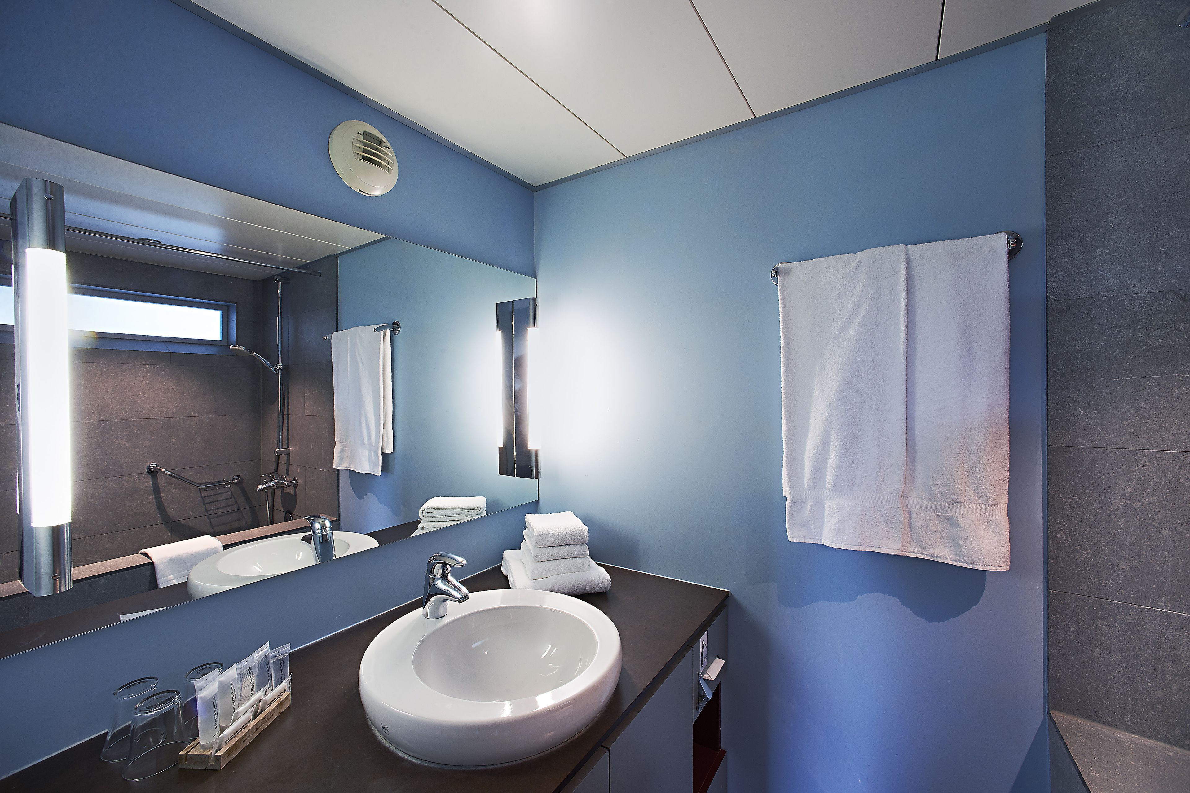 Un baño moderno con un lavabo grande, espejo y toallero.