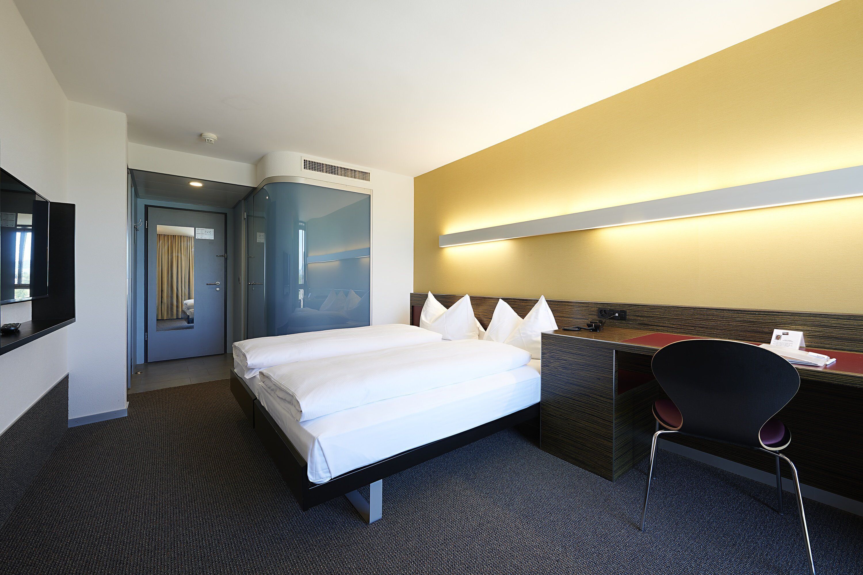 A hotel room with a bed, desk, chair, and a mirror.