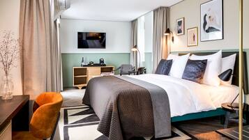 A modern hotel room with a large bed, a desk, a chair, a TV, and artwork on the walls.