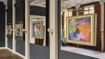 A hallway with framed abstract paintings on the walls, a wooden floor, and a ceiling with a grid pattern.