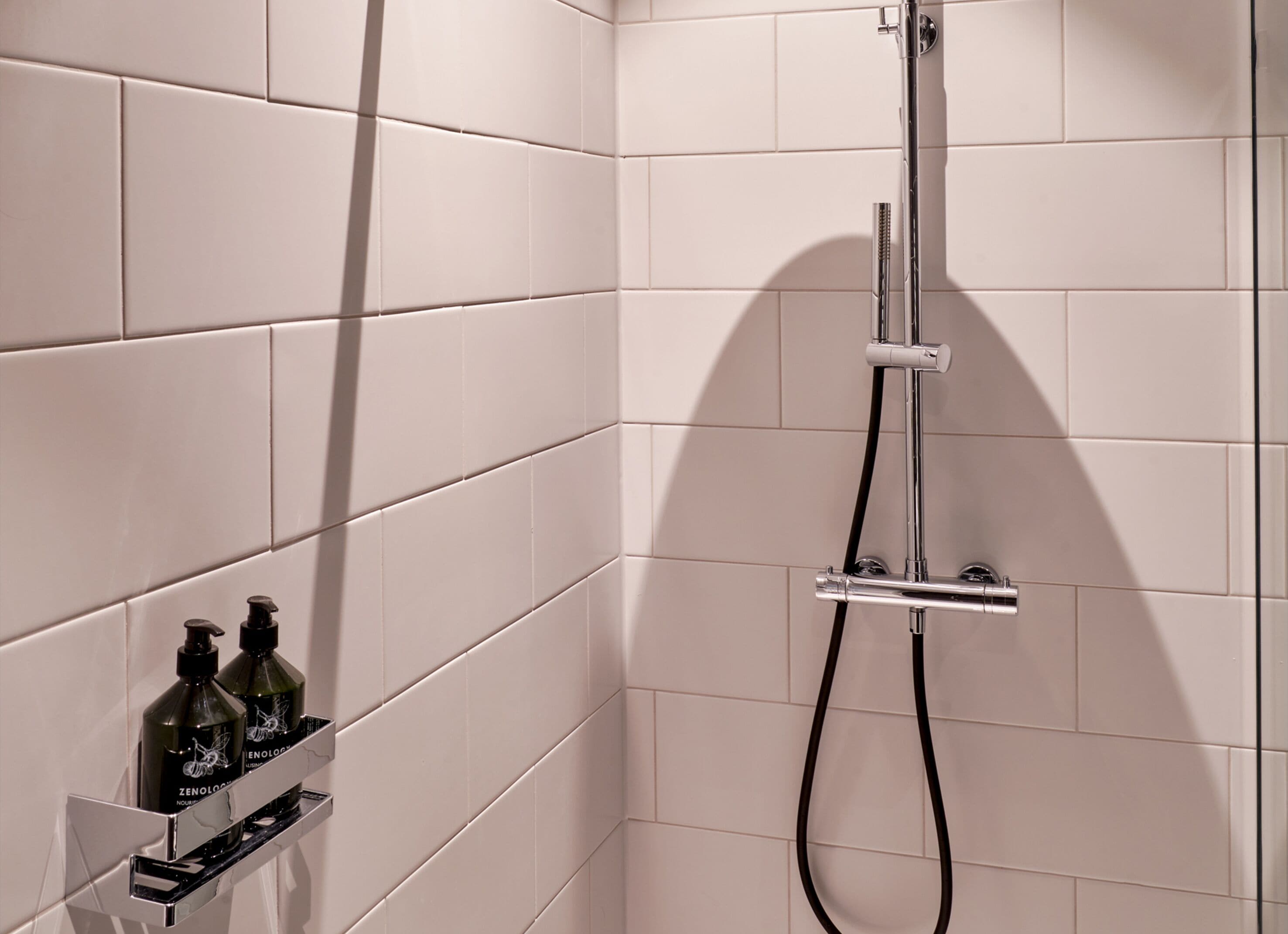 Une salle de bain moderne avec des carreaux blancs, une pomme de douche chromée et une étagère pour le distributeur de savon.