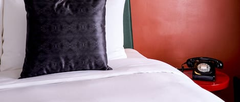 A bed with white linens, a black pillow, and a red telephone on a side table.