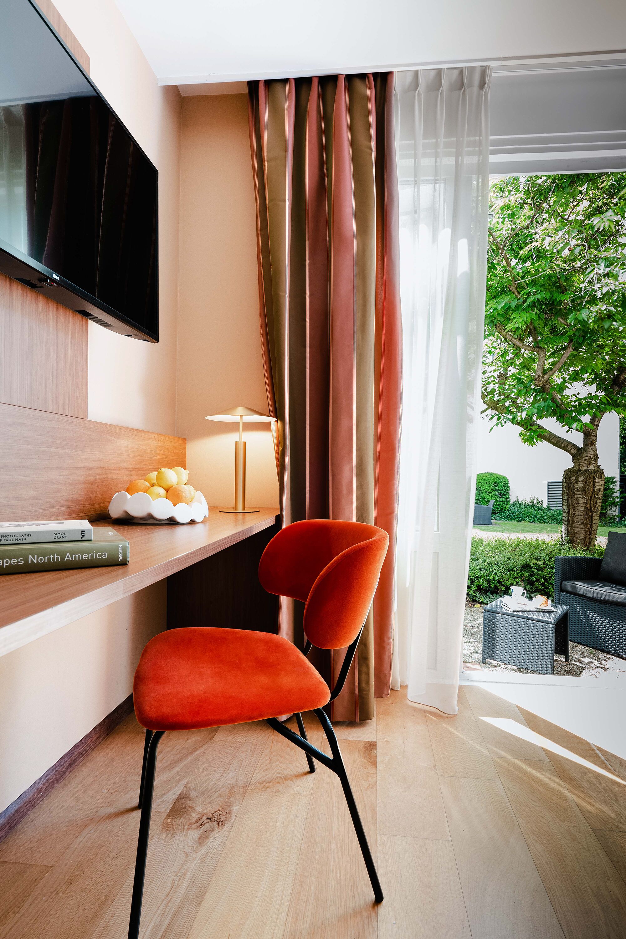 Una habitación de hotel moderna con una televisión de pantalla plana, un escritorio con lámpara, un frutero y una silla roja.