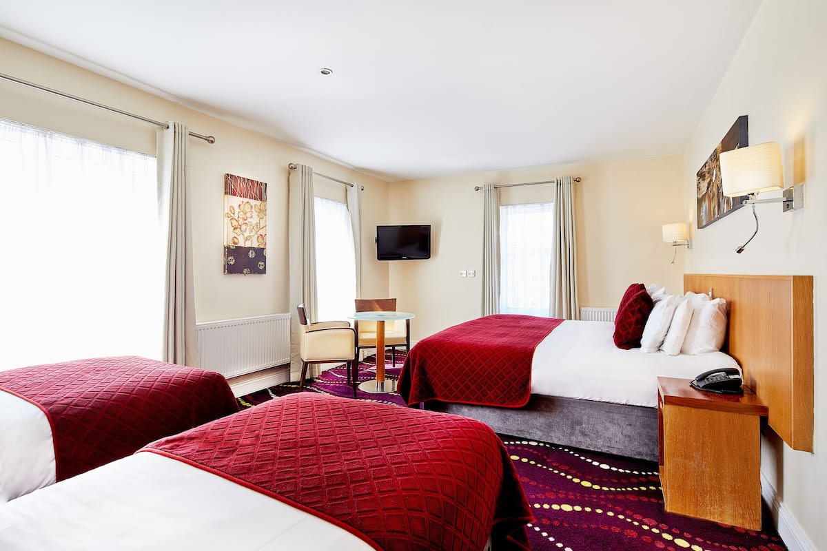 A hotel room with two beds, a small table, a chair, a TV, and a bedside table with a phone.