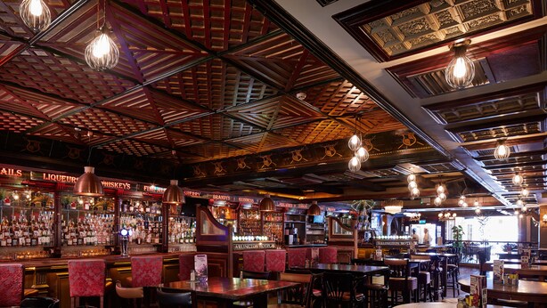 A bar with wooden ceiling and hanging light fixtures, bar stools, and a variety of liquor bottles. - Arlington Hotel O'Connell Bridge (Dublin)