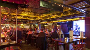 A crowded bar with wooden tables and chairs, a stage with a performer, and a patterned ceiling. - Arlington Hotel O'Connell Bridge (Dublin)