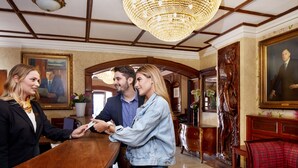 A reception area with a wooden reception desk, a chandelier, and a red upholstered sofa. - Arlington Hotel O'Connell Bridge (Dublin)