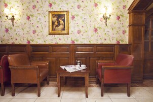 Een kamer met twee leren stoelen, een houten tafel met een krant en bloemenbehang.