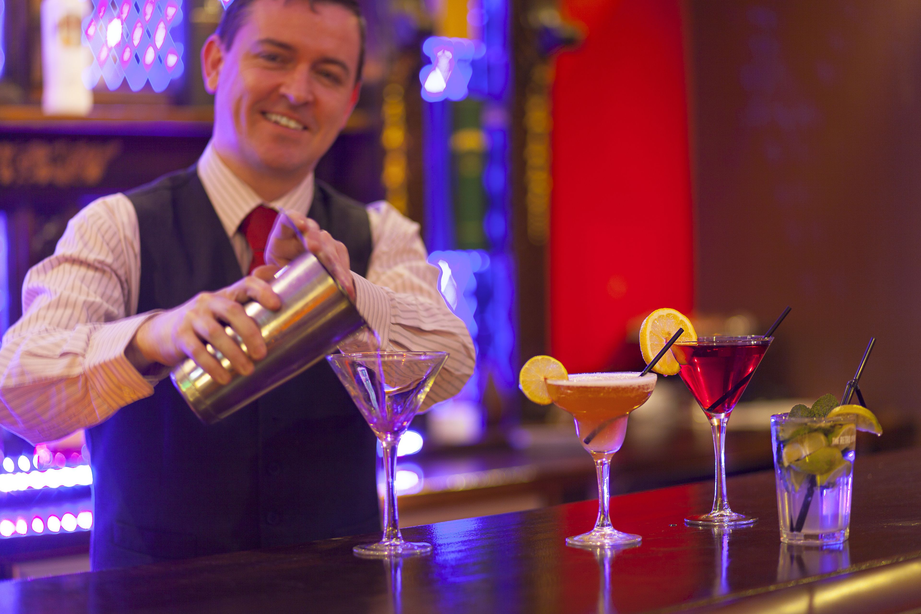 A bartender pouring a drink into a martini glass.