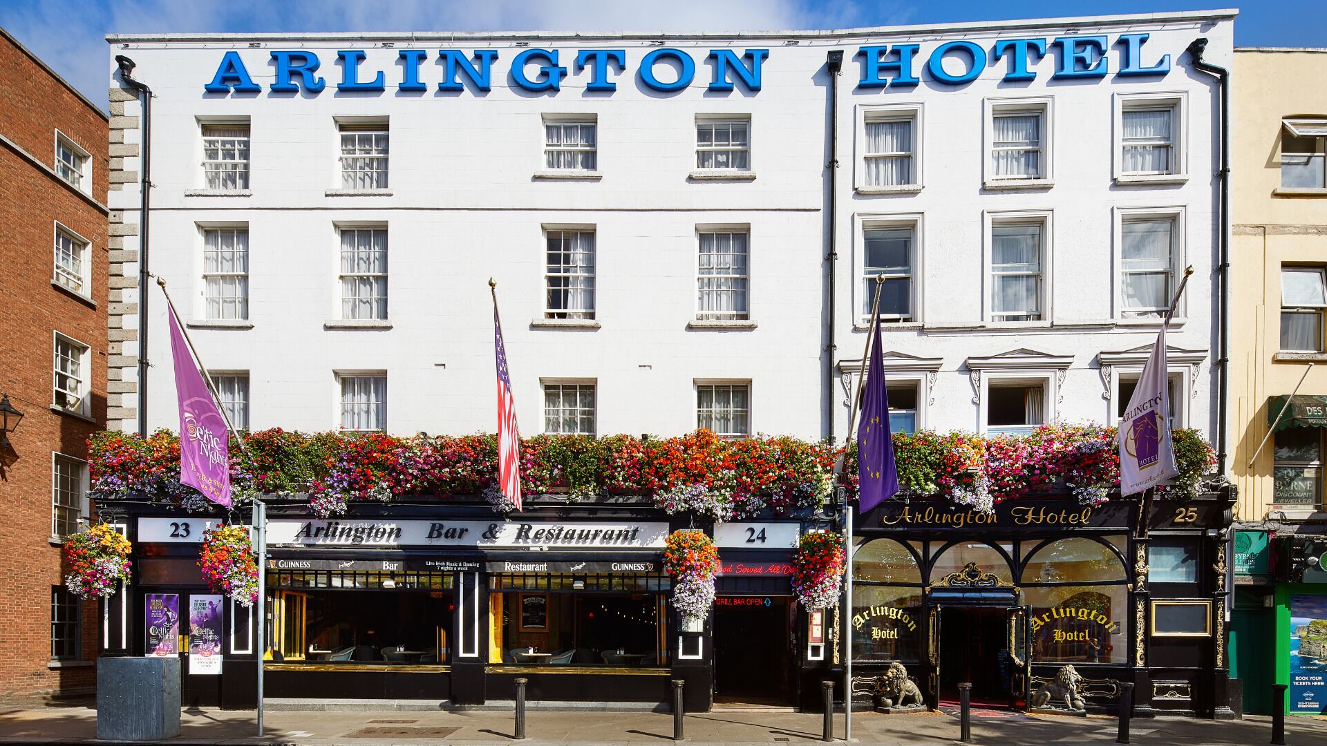 Esterno dell'Arlington Hotel con un bar e un ristorante al piano terra, bandiere e fioriere.