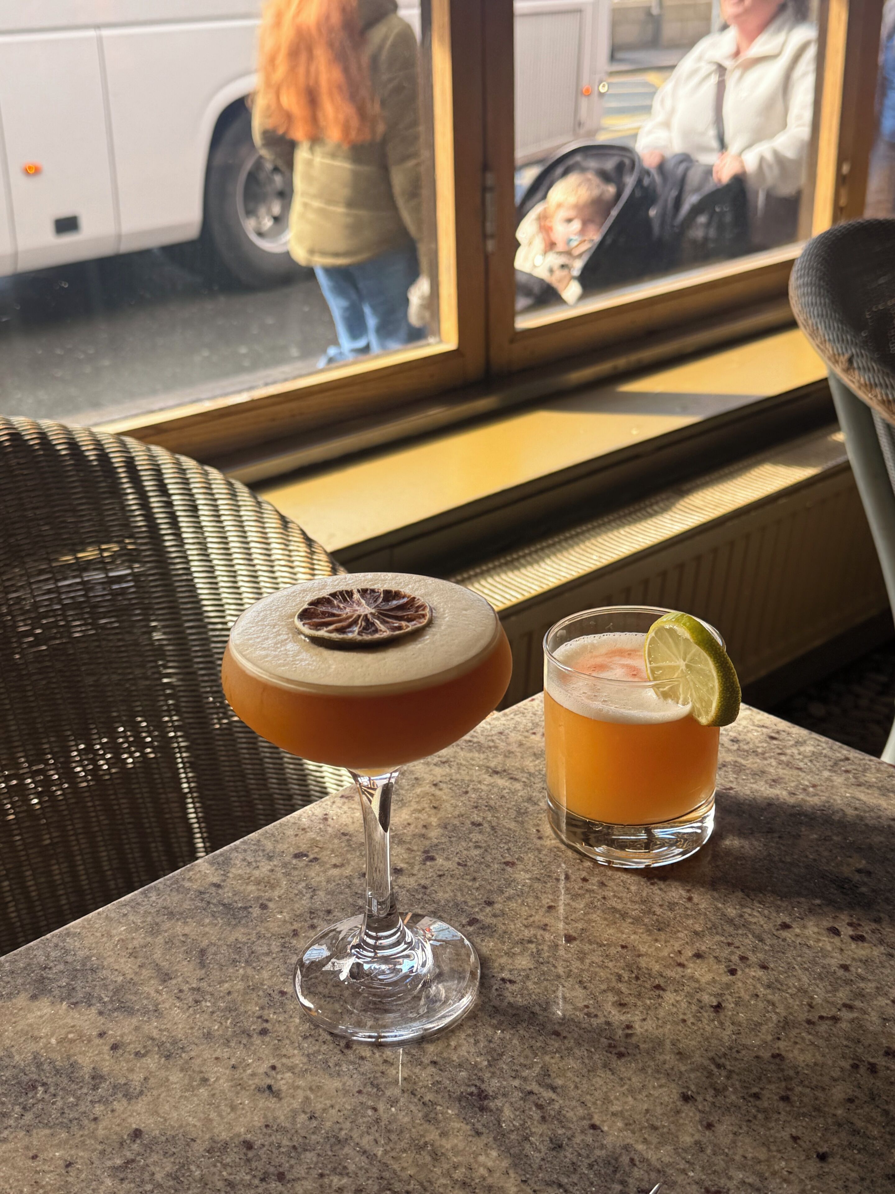 A bar area with a drink in a stemmed glass and a glass with a lime garnish.