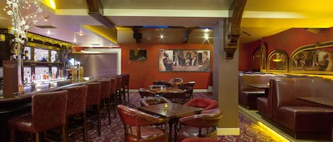 Un restaurant avec des tables en bois et des banquettes rouges, un bar avec des bouteilles exposées, et un mur orné de tableaux.