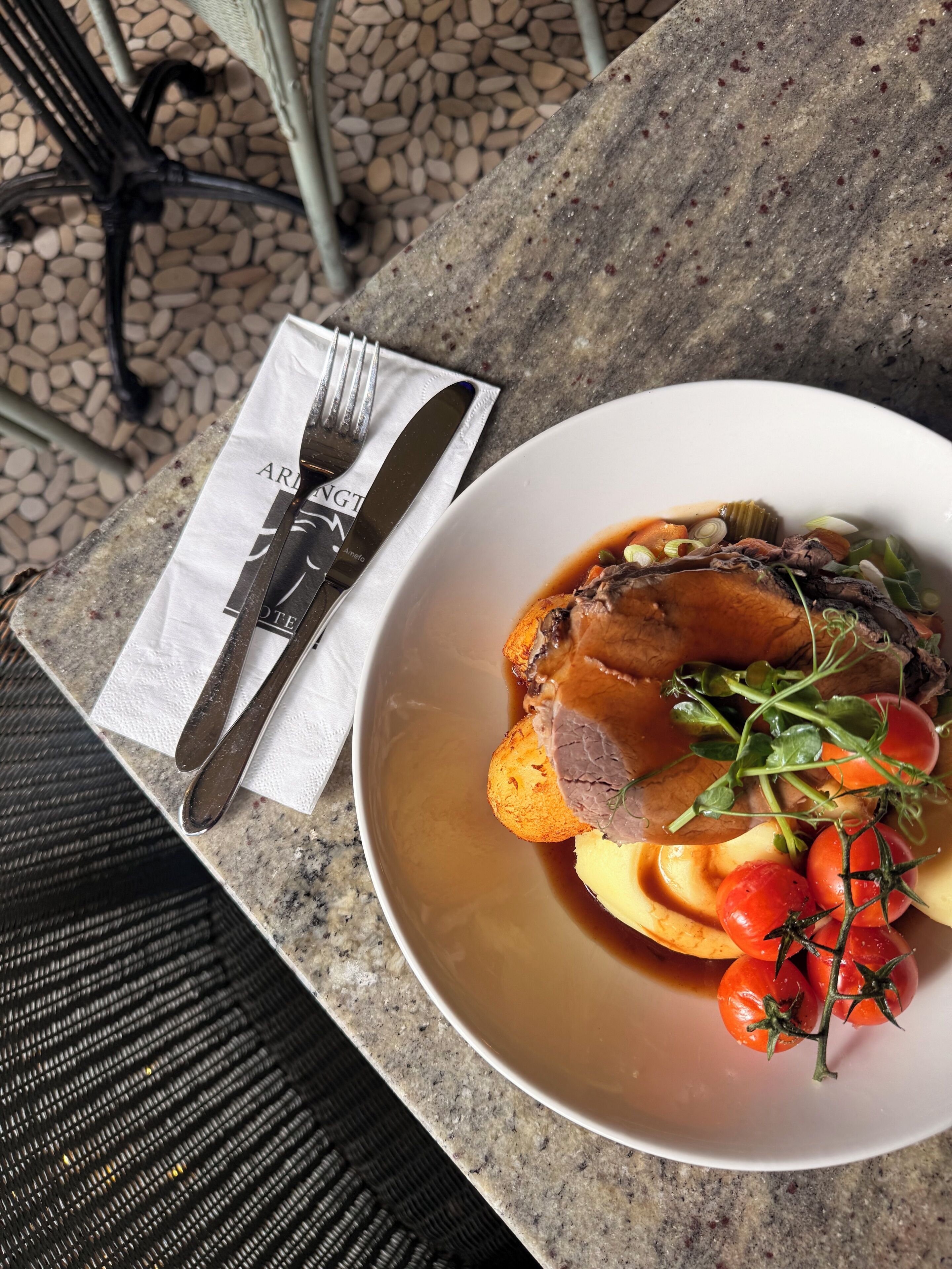 A plate of food with a fork and knife on a napkin, placed on a stone surface.