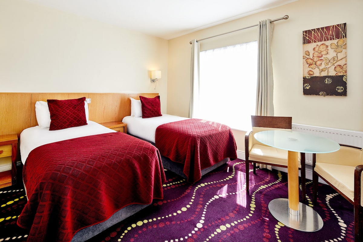 A hotel room with two beds, a round table, and a large window with curtains.