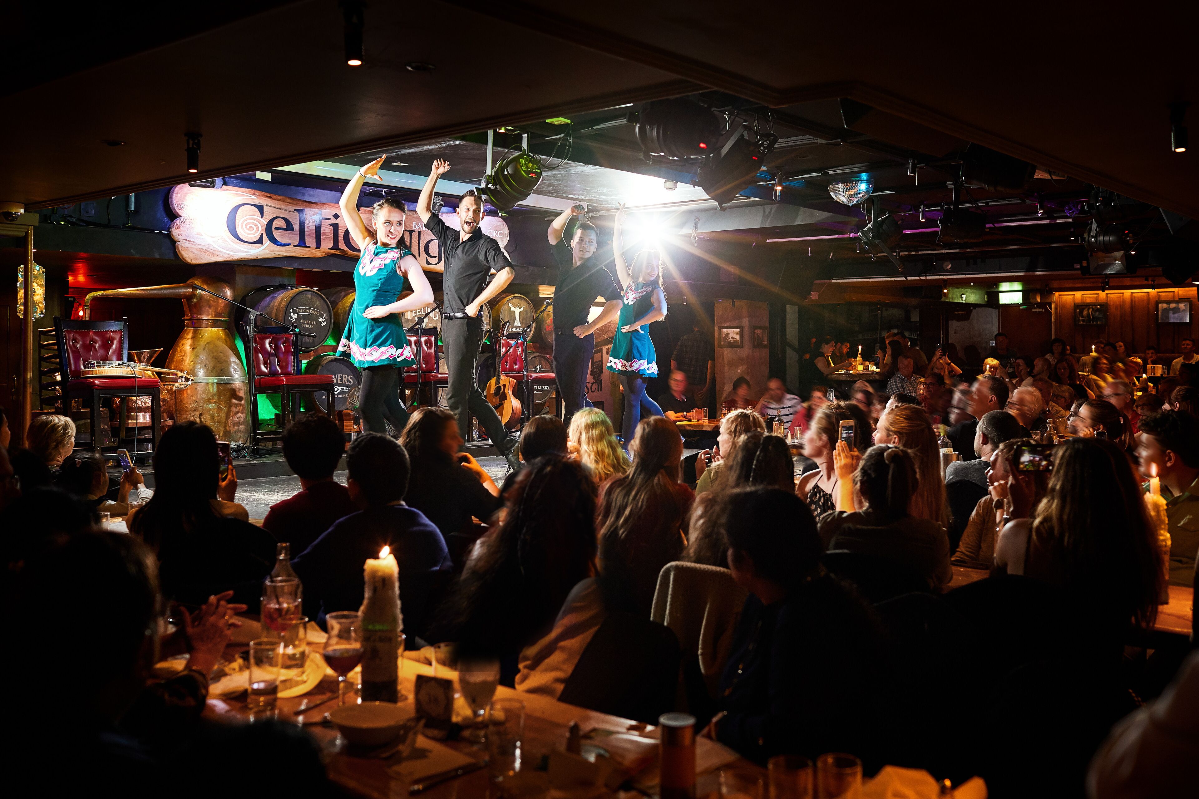 A crowded indoor venue with a stage, tables, and chairs.