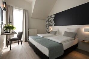 A modern bedroom with a bed, bedside tables, a desk with a chair, and a window with curtains. - Martin's Brugge (Bruges)