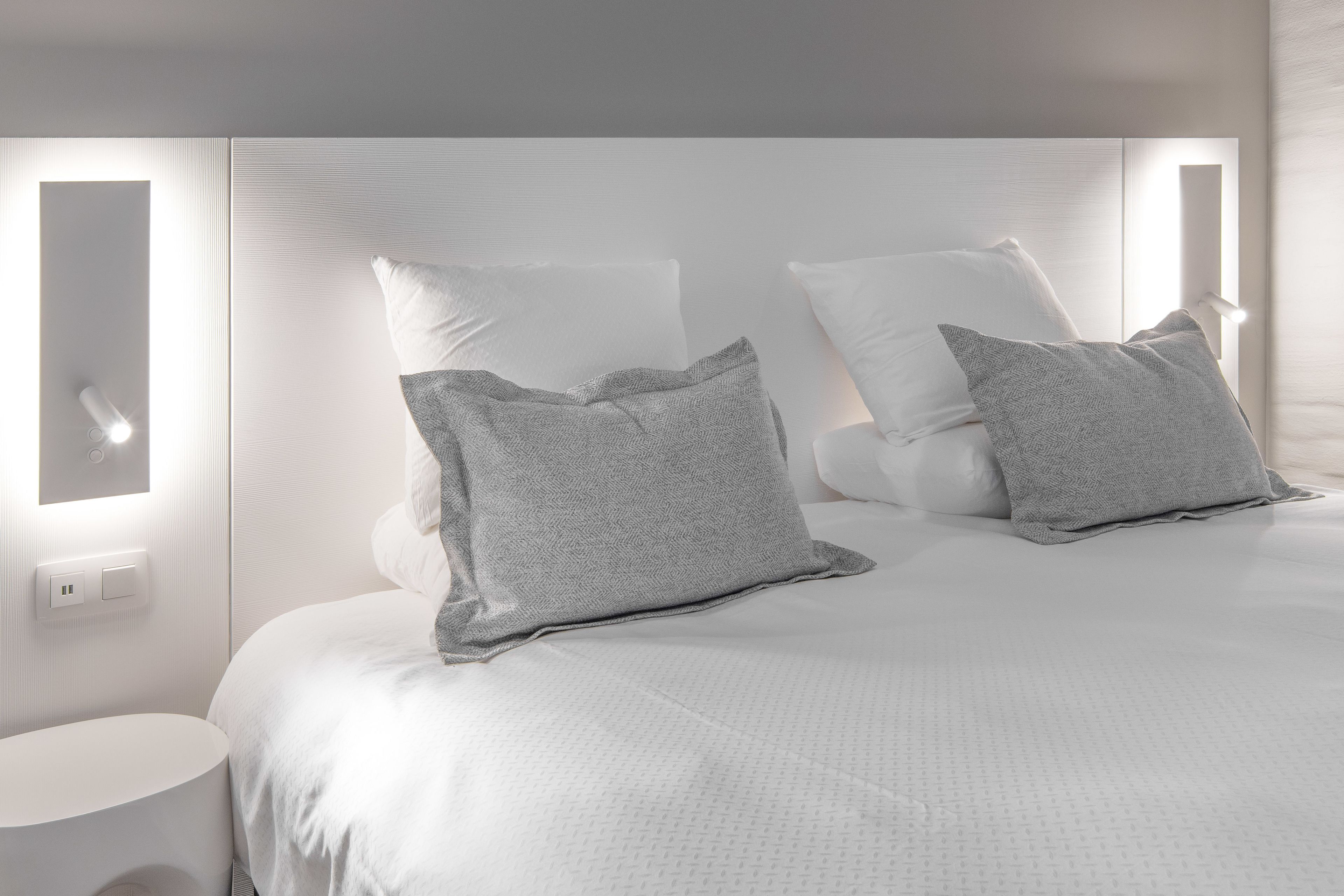 A modern bedroom with a large bed, two bedside tables, and a wall-mounted light fixture.